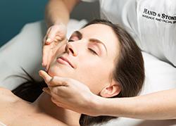 Woman with her head back and eyes closed receiving a facial from a professional.